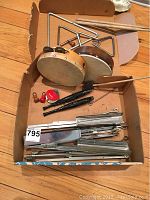 Box of musical instruments including 2 tambourines, 4 triangles with beaters, 2 black recorders, and 5 folded music stands in a box.