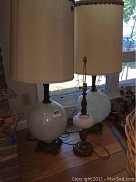 Side view of the three lamps, showing two large spherical white glass lamps with cream-colored shades and one smaller lamp without a shade featuring wood and white glass base.