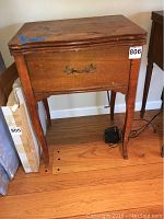 Front view of vintage wooden cabinet for Singer sewing machine showing antique brass handle and tapered legs.