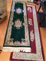 Two floral design rugs, dark green runner on top of a large burgundy floral bordered rug, wooden floor