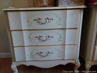 Front view of the end table showing three drawers with floral painted decoration and silver-tone handles.