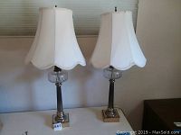 Pair of matching table lamps with metal and glass details, white scalloped shades, 33 inches tall.