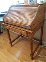 Closed view of the wooden roll top secretary desk showing slatted roll-top and turned legs.