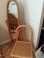 Full view of the floor mirror with wooden frame and arched top alongside the cane bottom chair in a corner.