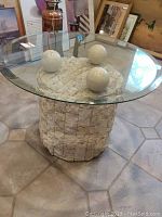 Front angled view of coffee table showing glass top and textured base with three spherical elements.