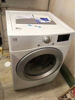 Full view of white front-loading dryer showing top surface, door and surrounding area