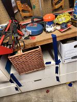 Workbench drawers and basket containing additional supplies below the bench surface with mounted saws visible.