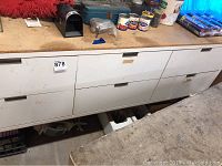 View of white six-drawer workbench with wood top, showing drawers closed with some items on top and around.