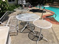 White metal outdoor furniture set including bench and two round tables by poolside on concrete patio