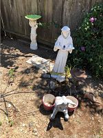 Overview of garden ornaments including tall white robed statue, pedestal birdbath with green dish, small dog statue, and plant pots.