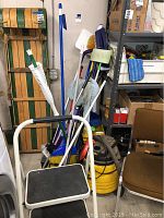 Cleaning tools including brooms, mops, dustpans near brown chair and shelving unit