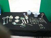 Full overview of the serving and flatware set displayed on black cloth with green and white background.