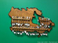 Front view of wooden wall mount shaped like Canada map with souvenir spoons hanging in two rows across four horizontal rails.