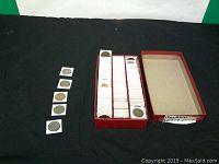 Box with red lid containing multiple rows of Irish coins in 2x2 coin holders, with some loose coins laid out beside it.