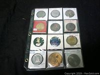 Front view of 12 medals and tokens in plastic sleeves arranged in a binder sheet, showing different designs, metals, and dates.