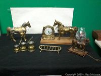 Overall view of horse figurines, clock, lamp, pouring containers, and rack on black cloth against white background
