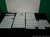 Overview shot of multiple 2x2 coin holders and folders containing Canadian nickels from 1922 to 1962 arranged on a black surface