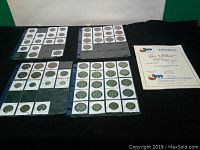 View of multiple coin collection pages with coins in 2x2 holders arranged in plastic binder sheets along with an auction book.