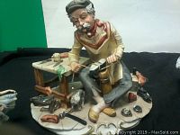 Seated cobbler figurine at workshop bench with tools and shoes