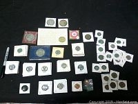 Overview of assortment of 97 vintage coins in sleeves and holders arranged on black surface next to marker for scale.