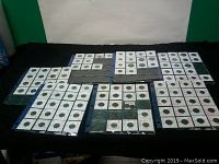 Photo showing seven sheets filled with numerous coins in clear protective holders laid out on a dark cloth. Coins are arranged in rows with visible handwritten details on each holder.