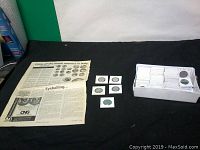 Overview of the lot showing the container with many wrapped coins, a few individual coins in holders, and printed material about coins of Greek colonies in Italy.