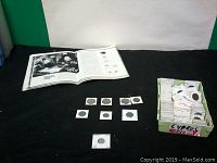 Overview of coins laid out on black cloth with a container holding multiple individually sleeved coins.