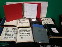 Front view showing an open red three-ring binder with some removable stamp pages, and multiple hardcover albums open to pages featuring printed stamps.