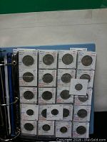 Blue binder open to plastic sleeves displaying 24 Mexican coins, each in labeled individual holders with handwritten year and details.