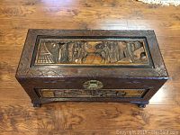 Top view of wooden chest showing carved panel with figures and buildings