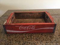 Front view of Coca-Cola wooden crate showing red paint with white 'Enjoy Coca-Cola' branding and metal corner reinforcements.