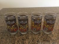 Four vintage Coca-Cola drinking glasses with colorful flower pattern displayed on countertop