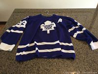 Front view of blue Toronto Maple Leafs jersey with white stripes and maple leaf logo on chest, size large.