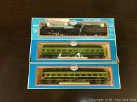 Three HO scale model train pieces in original Model Power boxes: one Puff-A-Smoke steam locomotive with tender and two Canadian National passenger cars.