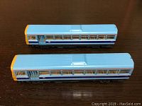 Top view showing two HO scale model street cars side by side on a wooden surface. Cars are painted light blue with window and door details.