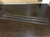 Eighteen HO scale flex track pieces laid out on a dark wood table, showing metal rails and black plastic ties.
