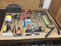 Photo of assorted hand tools spread on a table including pliers, staple removers, saws, planes, and clamps.