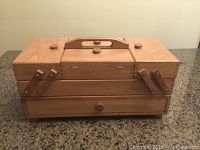 Closed rectangular wooden sewing box with top handle and knobs on top.