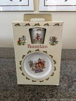 Front image of original Bunnykins-branded box showing cup and bowl through clear windows with character illustrations on box.