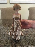 Photo of 1962 Midge Barbie in gold and white striped dress, held to show full figure and dress detail.