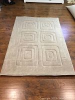 Full view of beige carpet rug with embossed square patterns on hardwood floor