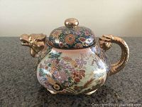 Front-side view of the Satsuma tea pot showing hand-painted floral designs and dragon-shaped spout and handle with gold-tone finish.