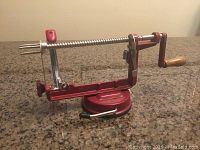 Side view of red and metal apple peeler showing wooden handle and suction base.