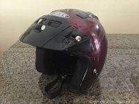 Side view of maroon Gmax motorcycle helmet with black visor, showing foam and strap interior.
