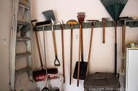 Photo of garden tools hanging on rack including shovels, rakes, and axe showing full lot