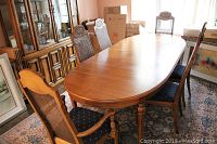 Dining table surrounded by 6 cane back wood dining chairs with dark fabric upholstered seats, 1 captain chair with armrests visible