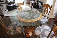 View of round glass top dining table with wood and ornate metal octagonal center and four floral fabric upholstered wood chairs