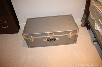 Front and top view of gray Seward storage trunk showing latch, clasps, and riveted metal reinforcement