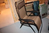 Photo of one gravity lounge chair fully open with tan fabric and black metal frame, showing armrests and headrest.