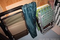 Two green fabric carrying bags containing outdoor event folding chairs, alongside lightweight folding chairs with woven plastic straps and metal frames.